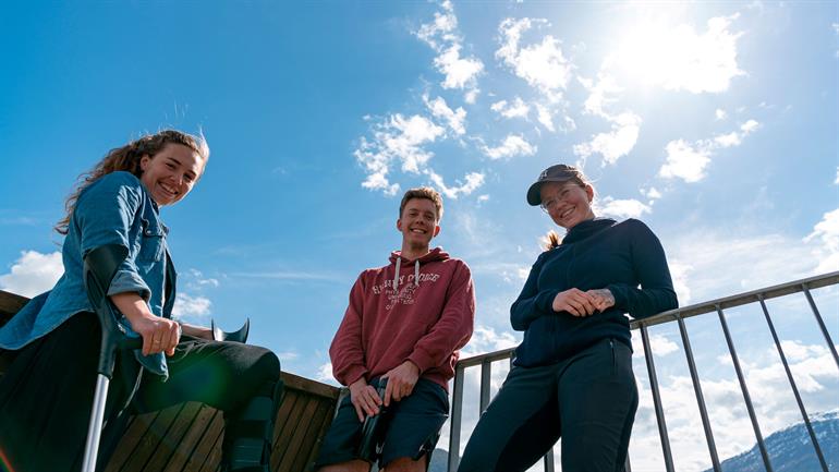 Tre blide studentar og blå himmel.